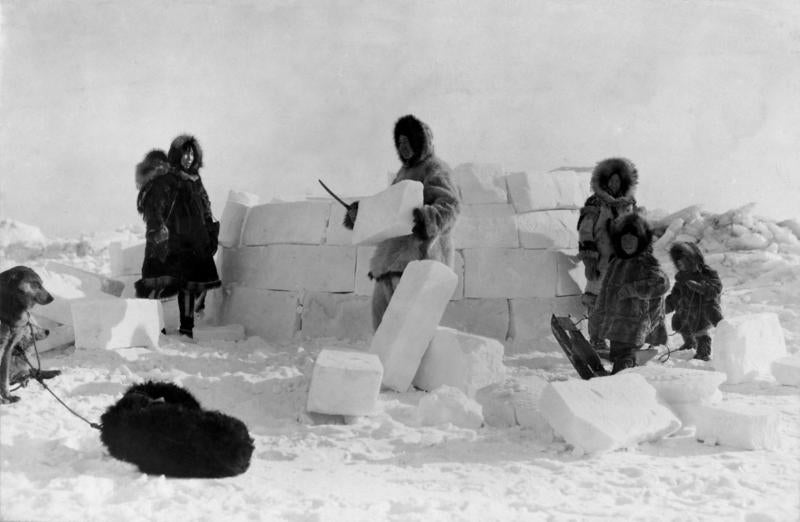 An Inuit family working together to build an iglu using snow blocks.