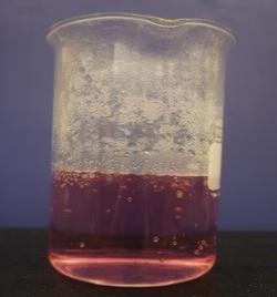 A beaker with a clear light pink solution.