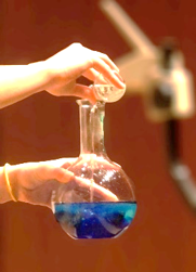 A woman pouring a solution from a beaker to a round bottom flask.
