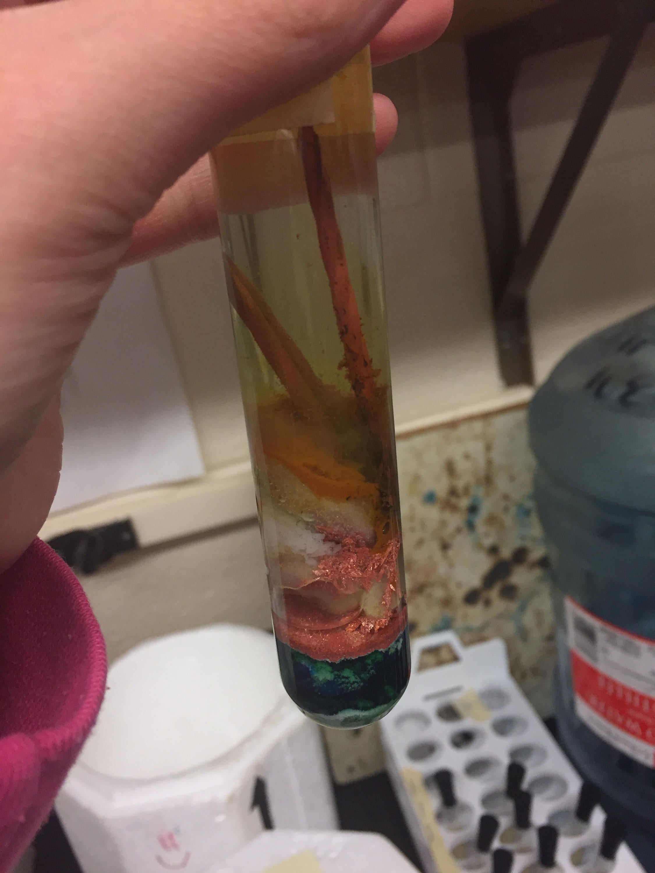 Three layers in a test tube with a bottom dark green layer, a copper coloured middle layer and a brownish cloudy solutions with two nails  not present