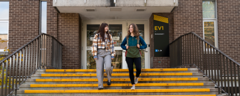 Two smiling students descend the stairs of Waterloo's Environment 1 building wearing autumnal clothing