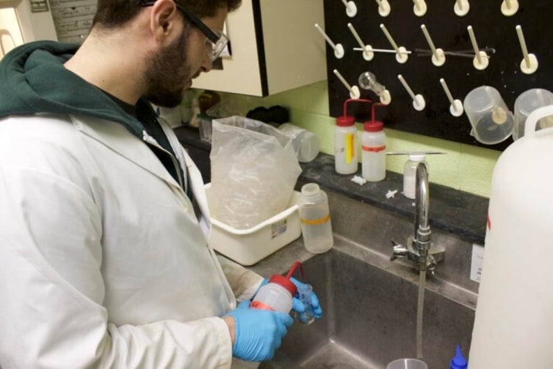 Student in lab coat standing at sink pipetting liquid into small test tube