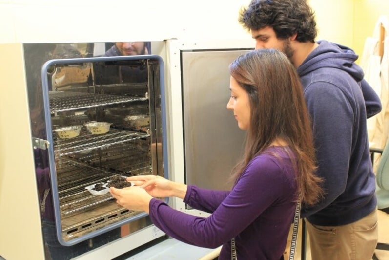 Student placing small dish of soil into an oven