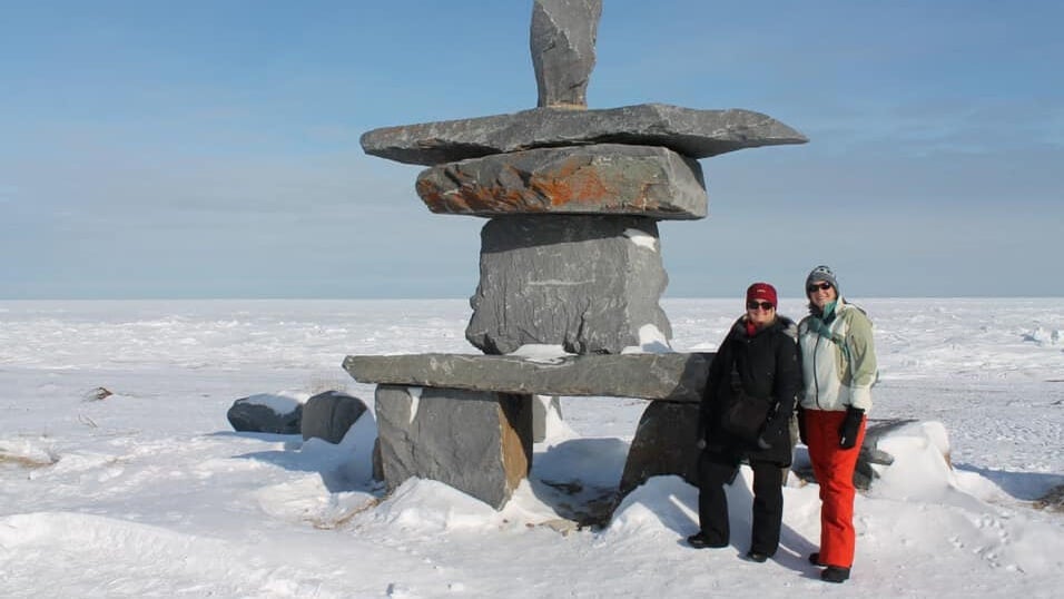 Two women standing by a large inukshuk