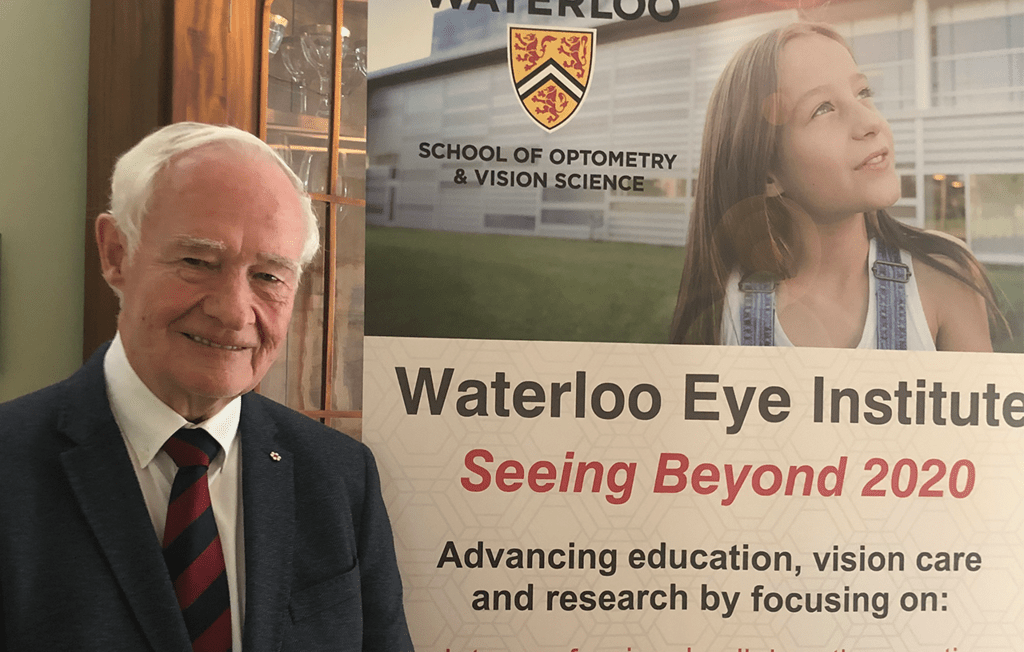The Right Honourable David Johnston stands in front of a banner for the Waterloo Eye Institute.