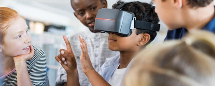 Child wearing virtual reality headset as other kids watch.