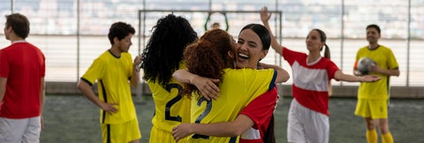 Two soccer players on opposing teams hug each other at end of game.