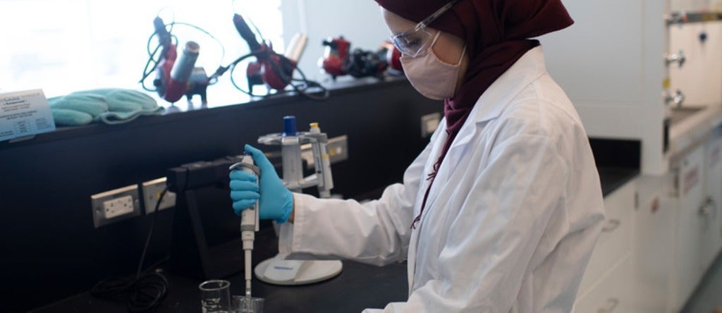 Researcher in lab coat holding syringe.
