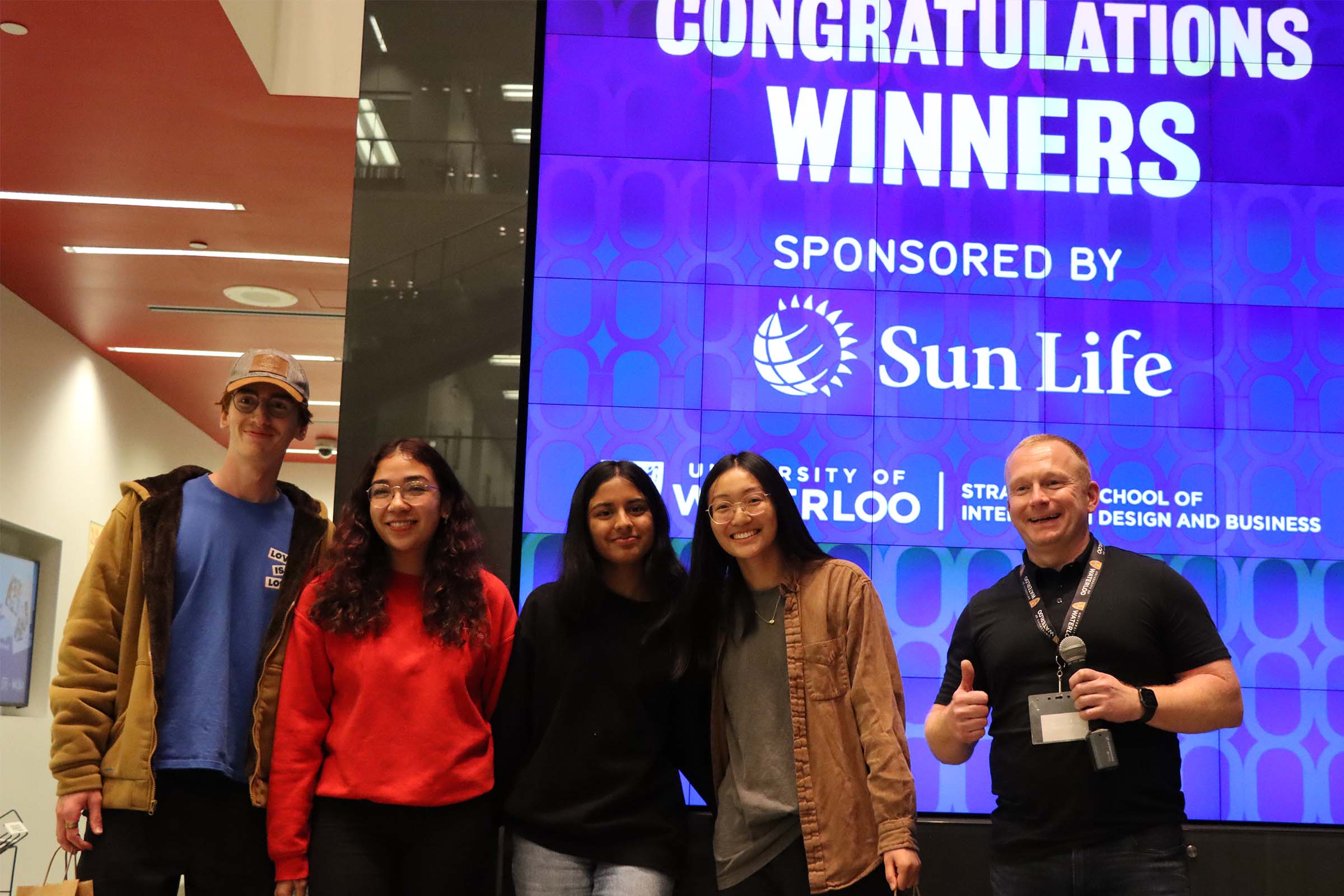 Runner up team of GBDA students and Sun Life representatives pose in front of the Wall that says "Congratulations Winners"